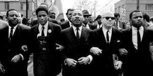 mlk: martin luther king jr. linking arms with other men in a black and white photo