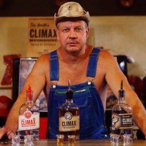 Moonshiners: man in overalls and no shirt with a cowboy hat in front of liquor bottles