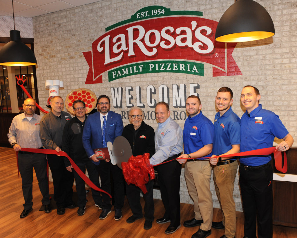 group of people standing in front of a LaRosa's sign with ribbon