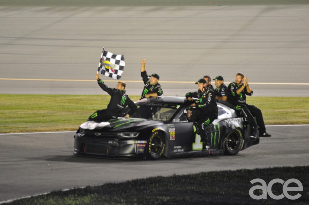 Kurt Busch holing the checkerd flag and team riding on the No. 1 Monster Energy Car.