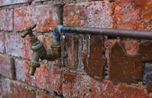 outdoor water spiket with icycles hanging on it with a brick background
