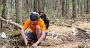 environmental: man in an orange shirt and hat digging in the ground