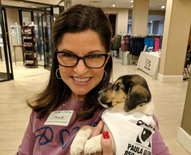 a woman holding a small puppy that is wearing a bandana