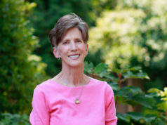 woman in pink shirt smiling with greenery behind her
