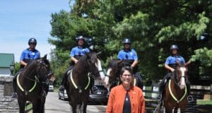 police officers on horses with a woman in an orange jacket standing in front of them