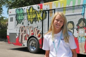 girl in a white polo smiling in front of a bus