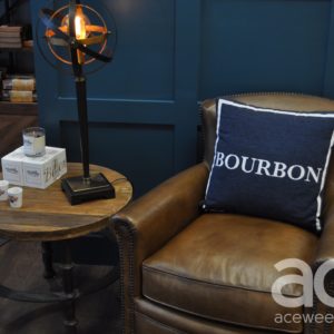 Joseph-Beth: brown leather chair with a pillow that says bourbon and a side table with lamp