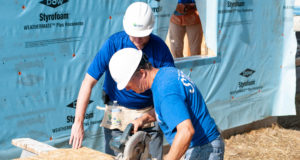 two men wearing blue shirts and white hard hats building
