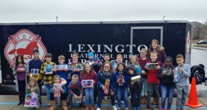 Toy Drive: kids holding toys standing in front of a trailer that says Lexington Fraternal order of Firefighters